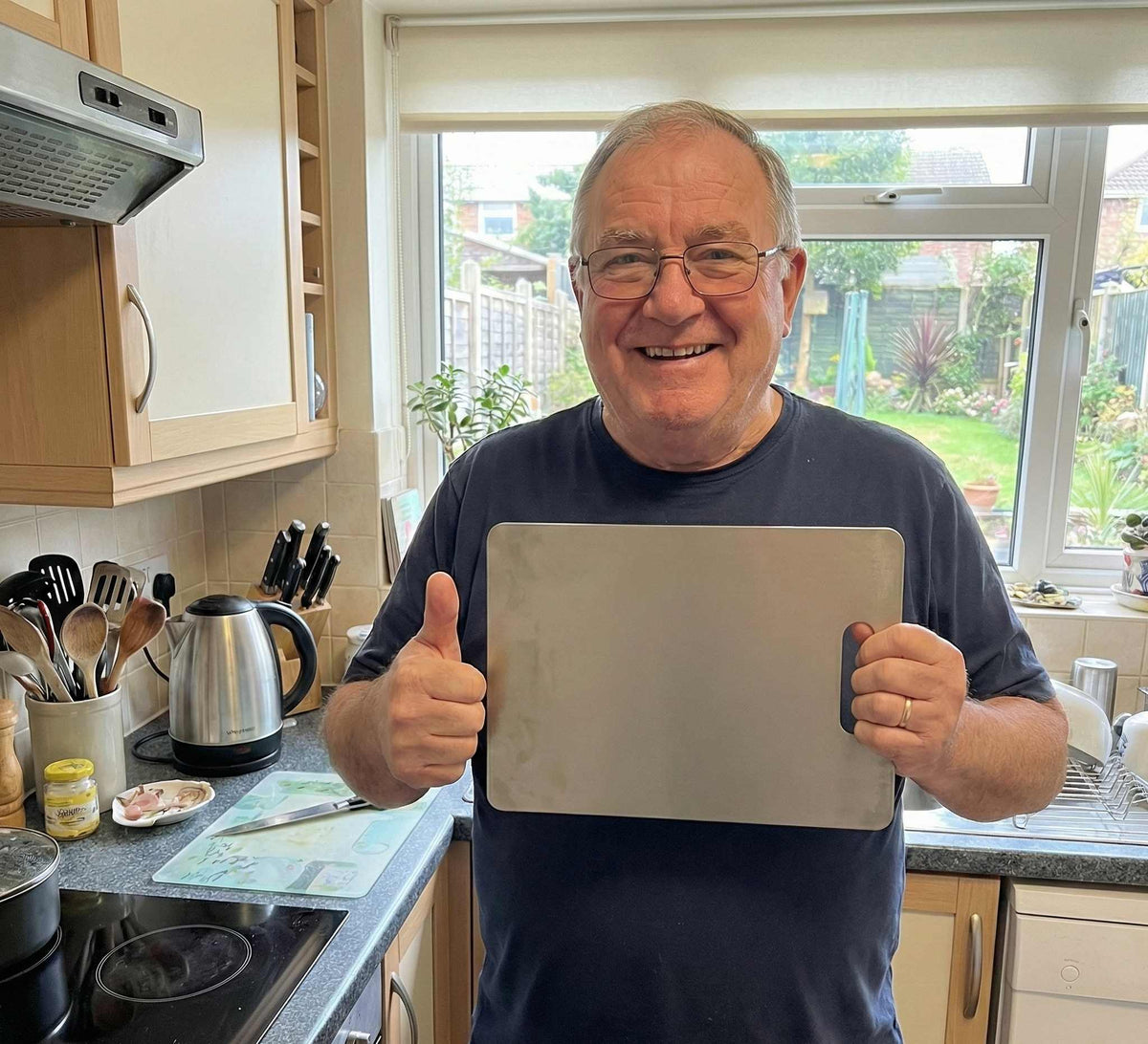 Smiling customer in a home kitchen giving a thumbs up review for the Life Upgrade Co titanium chopping board.